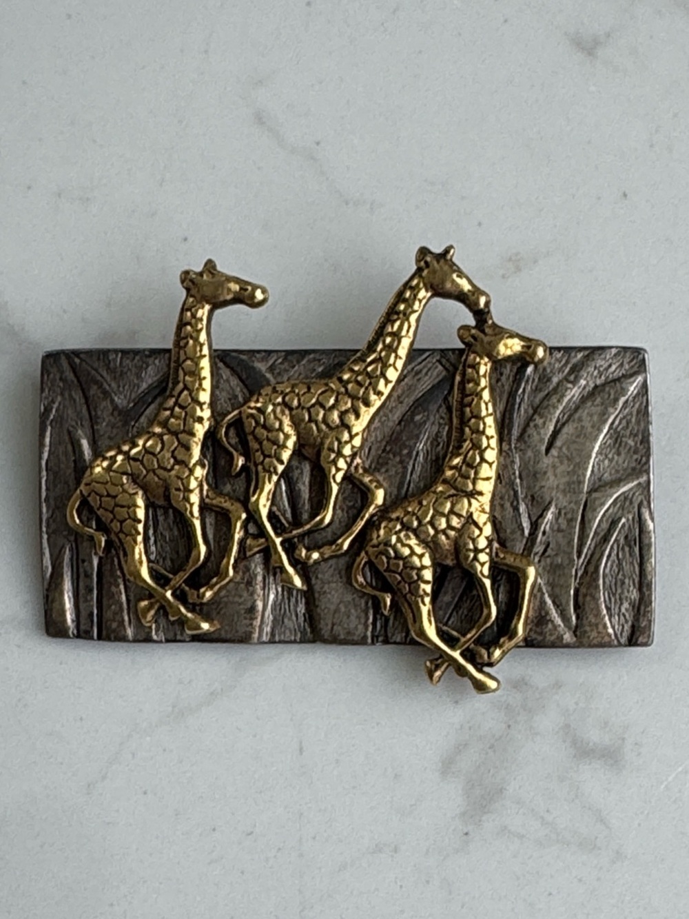 Darlene metal brooch featuring three running giraffes in gold and silver tones.